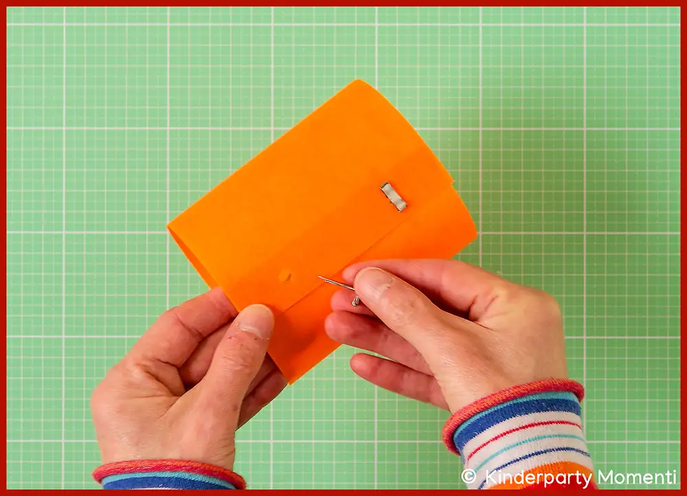 Hände verschließen mit Musterklammern eine orangefarbene Windlichter Banderole