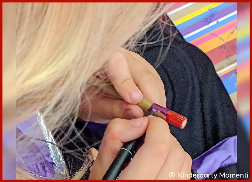 Hexen Zauberstab bemalen beim Kindergeburtstag Kind mit Hexenkostüm malt mit rotem Stift auf einen Zauberstab aus Holz an