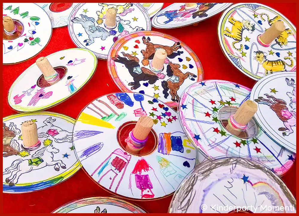 Zirkus Kreisel basteln mit CDs Mehrere selbstgebastelte Kreisel aus CDs mit bunten Zeichnungen von Tieren, Sternen und anderen Motiven, jeweils mit einem Holzstift als Griff in der Mitte